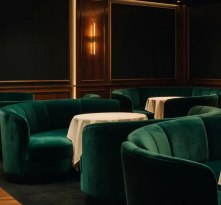 Elegáns lounge enteriőr esti fényekkel, dióbarna burkolatokkal és smaragd zöld kárpitokkal.